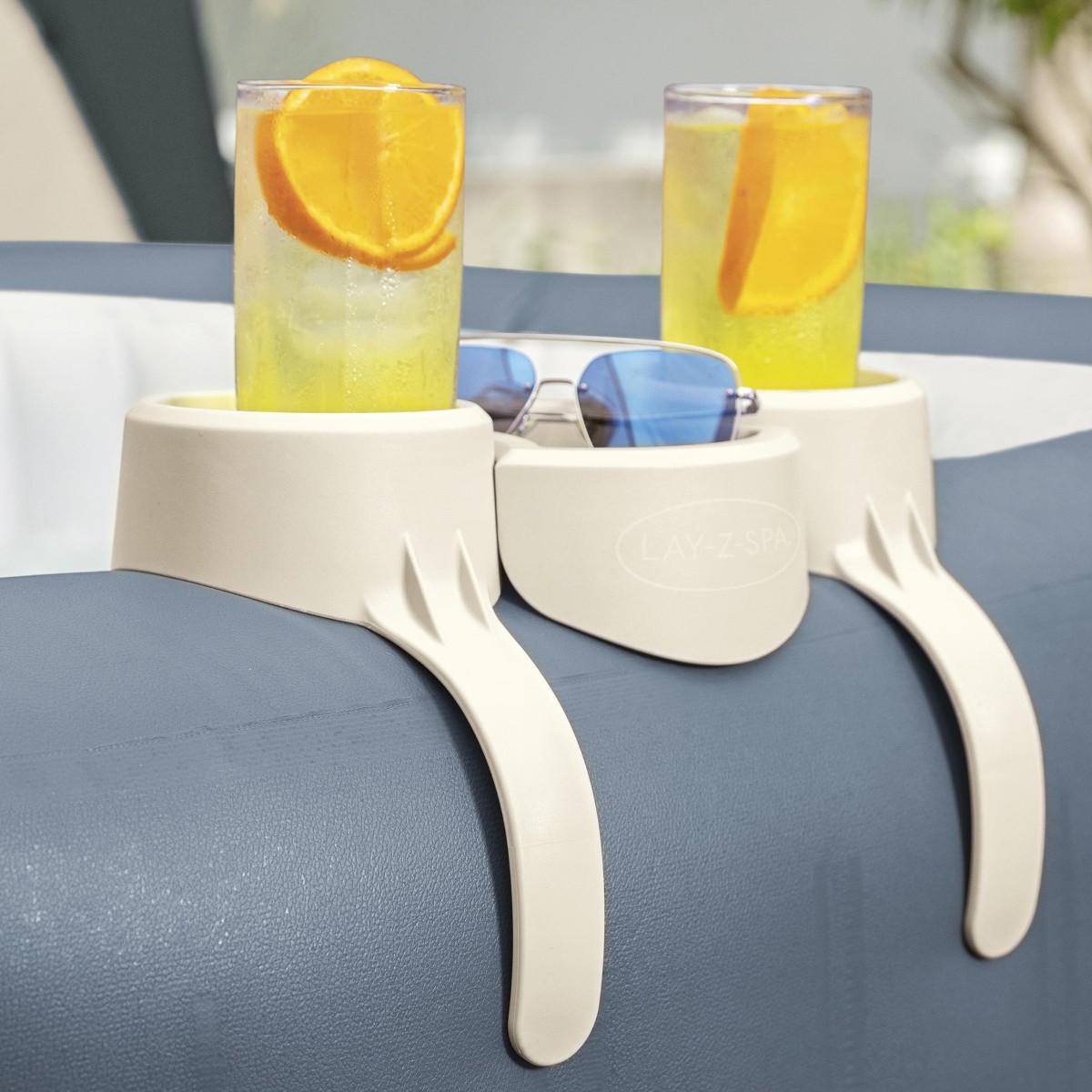 Uchwyt na napoje Lay-Z-Spa zamontowany na krawędzi jacuzzi, trzymający dwie szklanki z sokiem i okulary przeciwsłoneczne.